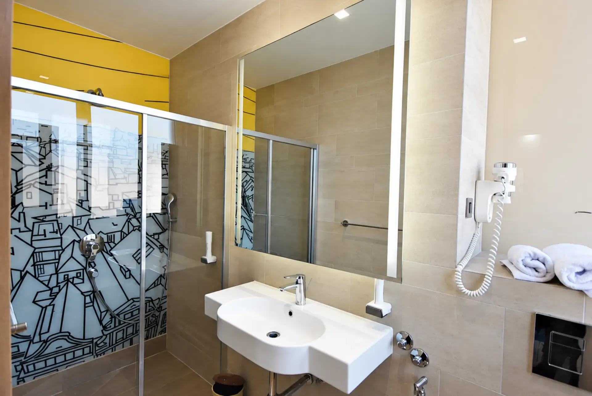 Guest bathroom at Hotel Cosmopolit with glass shower, wall hairdryer and folded towels